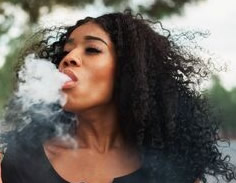 Tonnesha, a Black teen with long curly black hair breathing out smoke.