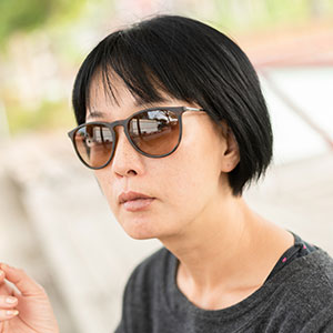 Linn is an 60-something Chinese woman with ear length black hair. She wears large sunglasses and a black shirt.