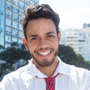 Silvio is a 20-something Brazilian man in a white dress shirt and red tie. He has short wavy hair, and a five o'clock shadow