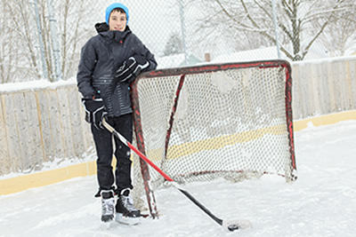 A teenager playing hockey outside on a ice rink